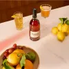 A bottle of Hennessy VSOP cognac is displayed on a white marble countertop with a glass of drink, lemons, and grapes. Produktbild-Vorschau