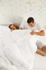 A couple is playfully interacting with a duvet on a bed. Voir les images du produit