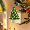 A ceramic Christmas tree night light plugged into a wall socket, surrounded by festive decorations and fairy lights. Náhľad obrázku produktu