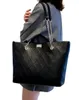A person is holding a black quilted tote bag. Náhľad obrázku produktu