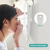 A woman is applying a contact lens in front of a mirror that is hanging on a wall. Podgląd zdjęcia produktu