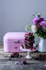 A pink Wesco bread bin is shown on a wooden table with a stack of brownies and a bouquet of flowers. Anteprima dell’immagine prodotto