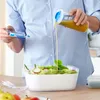 A person is pouring salad dressing from a container into a salad bowl. Anteprima dell’immagine prodotto