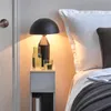 A bedside table with a lamp, a bottle of water, and a glass of water next to a bed. Produktbild-Vorschau