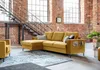 A modern living room with industrial-style decor, featuring a yellow sectional sofa, a metal staircase, and exposed brick walls.