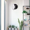 A wall clock with a hidden compartment for watches is mounted on a white wall, next to a shelf with plants and decorative items. Voir les images du produit