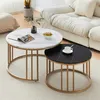 Two round coffee tables with marble-effect tops and gold metal frames are placed on a carpet in a living room setting, with a sofa in the background. Produktbild-Vorschau