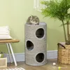 A cat is resting on top of a cylindrical cat tree with multiple openings, placed in a room with light green walls and wooden furniture. Produktbild-Vorschau