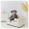 A large teddy bear sitting on a small sofa in a room with minimalist decor. Podgląd zdjęcia produktu