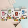 Four colorful digital music players in their packaging, arranged in a row on a light pink and blue background. A small Eiffel Tower figurine is placed in the foreground. Produktbild-Vorschau