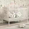 A white baby crib with bedding and pillows, set against a wallpaper with a forest and deer motif. Náhľad obrázku produktu