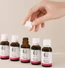 A hand is holding a white cap above a row of small brown bottles with white labels. Produktbild-Vorschau