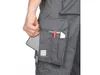 A close-up shot of a person's hand reaching into a pocket of gray work pants, showing the details of the pocket and its contents. Náhled obrázku produktu