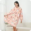 A woman is wearing a pink hoodie blanket with a rabbit pattern, standing in a room with a sofa. Náhled obrázku produktu