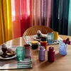 A table setting with breakfast items and colorful sheer curtains in the background. Produktbild-Vorschau