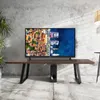 A television is placed on a wooden table in a room with a concrete wall. Produktbild-Vorschau