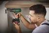 A man is using a cordless drill to attach a cabinet hinge. Produktbild-Vorschau
