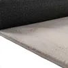 A close-up view of the underside and edge of a beige rug, showing its texture and the black, patterned backing. Produktbild-Vorschau