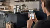 A person is using a smartphone to control a coffee machine in a modern kitchen. Produktbild-Vorschau