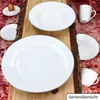 A collection of white porcelain dishes arranged on a wooden plank with a textured red background. Produktbild-Vorschau
