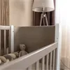 A close-up view of a baby crib with a teddy bear and braided bumper inside. Náhľad obrázku produktu