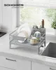 A dish drying rack filled with dishes, cups, and cutlery is placed on a kitchen countertop next to a sink, with a window in the background. Produktbild-Vorschau