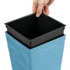 A hand is inserting a black plastic liner into a blue textured planter. Voir les images du produit