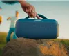 A blue Bose SoundLink Max speaker is placed on a rock in an outdoor setting with people in the background. Produktbild-Vorschau