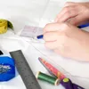 A close-up shot of hands using sewing tools on a white surface. Produktbild-Vorschau