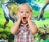 A young boy with a surprised expression is in the foreground, with a backdrop of dinosaurs. Podgląd zdjęcia produktu