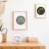 A collection of framed floral art and an embroidery hoop displayed on a wooden dresser. Produktbild-Vorschau