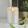 A close-up of a silver LED candle with a flickering flame, placed on a white surface with greenery in the foreground and background. Podgląd zdjęcia produktu
