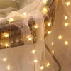 A string of star-shaped fairy lights draped over a sheer white fabric and a wicker chair. Náhled obrázku produktu