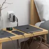 A Satechi USB-C charger is plugged into a wall outlet and charging multiple devices on a nightstand next to a bed. Náhled obrázku produktu