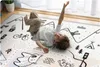 A young boy is lying on a play mat with a road pattern, mountains, and cartoon animals. Náhled obrázku produktu