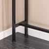 Close-up view of the black metal legs and base of a console table, resting on a dark wood floor against a beige wall and white baseboard. Podgląd zdjęcia produktu