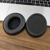 Two black ear pads for headphones are placed on a wooden surface next to a laptop. Podgląd zdjęcia produktu