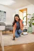 A woman is cleaning a carpet with a Kärcher washing vacuum cleaner in a living room. Produktbild-Vorschau
