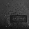A close-up of a black fabric surface with water droplets, featuring a black Eastpak logo patch. Voir les images du produit