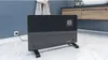 A black electric heater is placed on a marble floor in a bathroom setting, with a towel hanging on the wall and a vanity in the background. Náhľad obrázku produktu