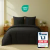 A bed with black bedding, two pillows, and a bedside table with a lamp and plant. Produktbild-Vorschau