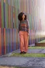 A woman stands in front of a colorful, striped wall. Produktbild-Vorschau