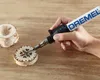A hand is using a Dremel VersaTip tool to woodburn a design onto a small wooden disc. Produktbild-Vorschau