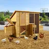 A wooden chicken coop with several chickens and chicks scattered around it on a bed of straw, with a garden and fence in the background. Produktbild-Vorschau