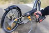 A person is using a cordless pressure washer to clean a bicycle wheel outdoors. Náhled obrázku produktu
