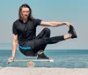 A man is performing a balance exercise on a balance board on a beach with the ocean in the background. Produktbild-Vorschau