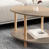 A close-up view of a modern oval coffee table with a two-tiered design, placed on a rug next to a sofa. The table has light-colored wooden legs and a cappuccino-colored top. Two books are stacked on the lower shelf. Voir les images du produit