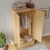 A light wood wardrobe with two doors, one open, revealing clothes on hangers and folded items on shelves. Two vintage suitcases and a brown duffel bag are on top of the wardrobe. A potted plant is to the left, and a rug is on the floor. Náhled obrázku produktu