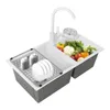 A double kitchen sink with a faucet, a dish rack with plates and cups, and a variety of fresh vegetables in the other basin. Podgląd zdjęcia produktu