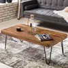 A wooden coffee table with hairpin legs sits on a patterned rug in a living room setting, with a sofa in the background.